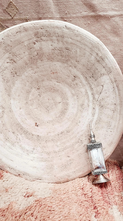 Unieke Marokkaanse Tamegroute schaal in naturel kleur, gestyled met zilveren parfumfles in een zacht interieur.