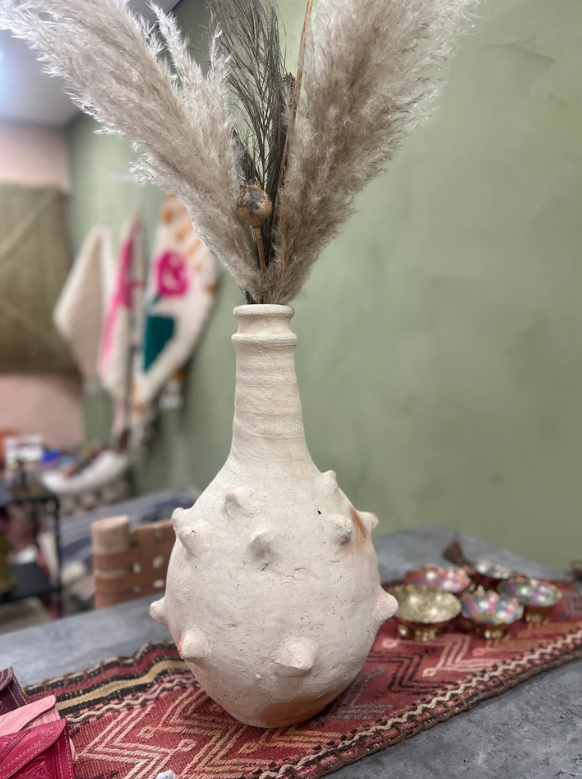Handgemaakte Marokkaanse vaas in naturel kleur, gestyled met warme textielaccessoires.