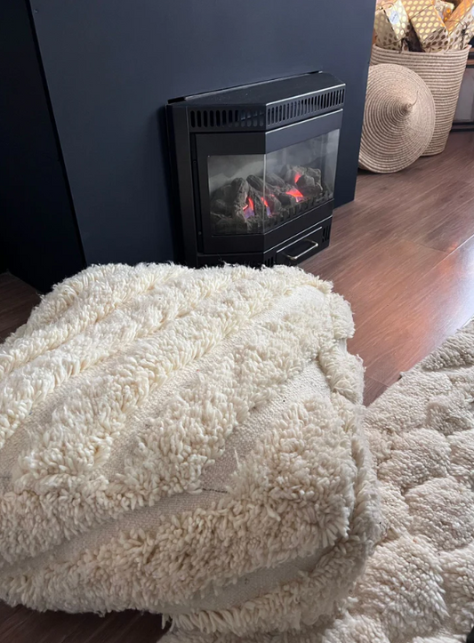 Sfeervol interieur met handgemaakte Marokkaanse poef van vintage textiel, geplaatst naast een open haard.