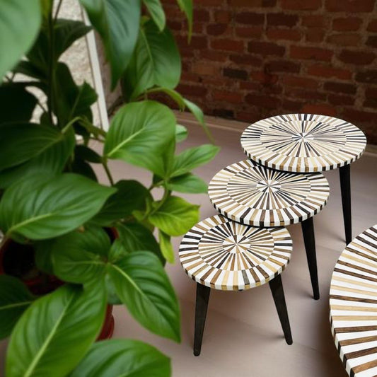 Set van drie lichte bijzettafels in walnoot en crème hars in botanische setting.